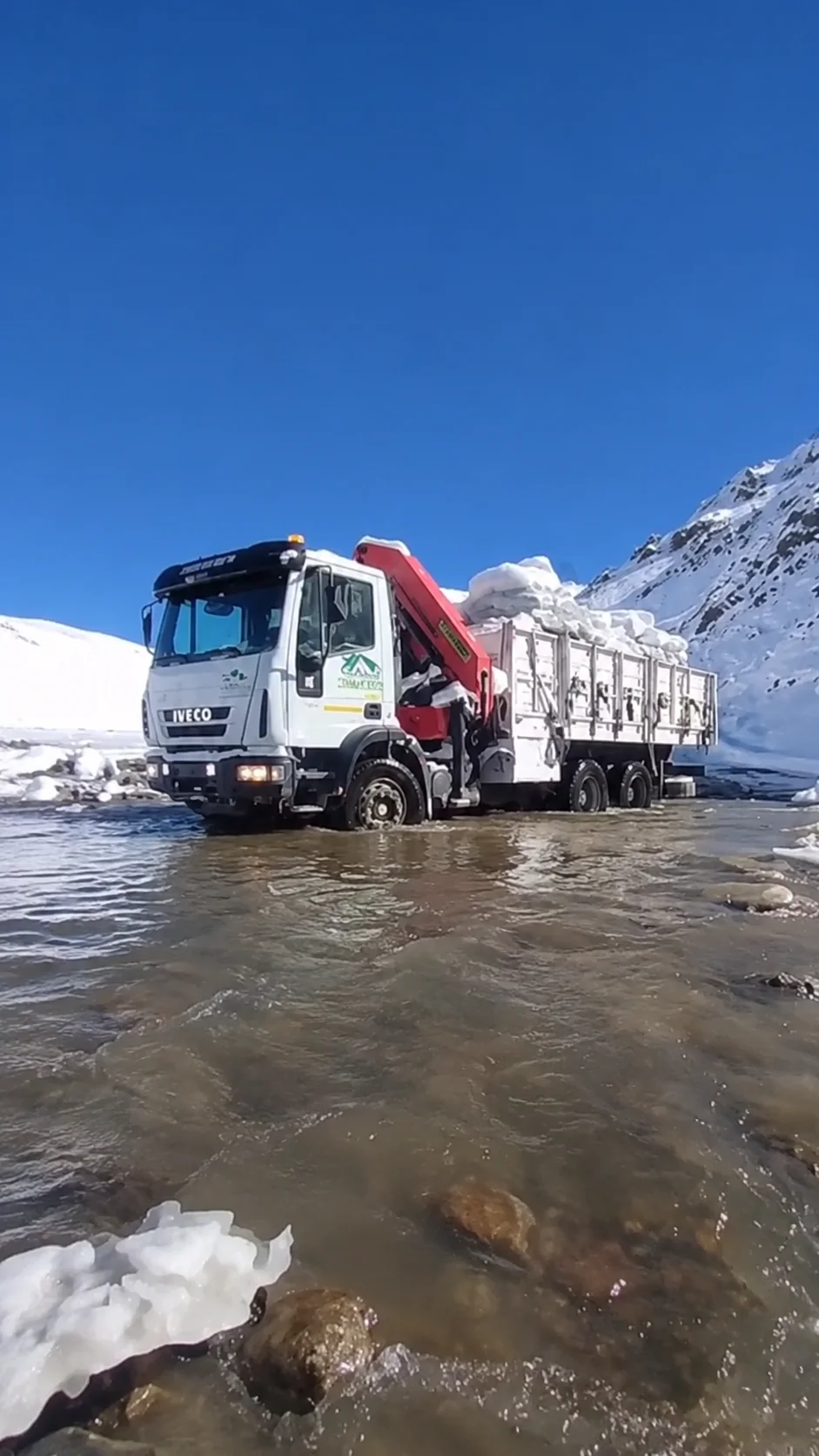 Camión con hidrogrúa de ISMAEL S.A. cruzando un río de montaña con nieve hacia un frente minero de San Juan